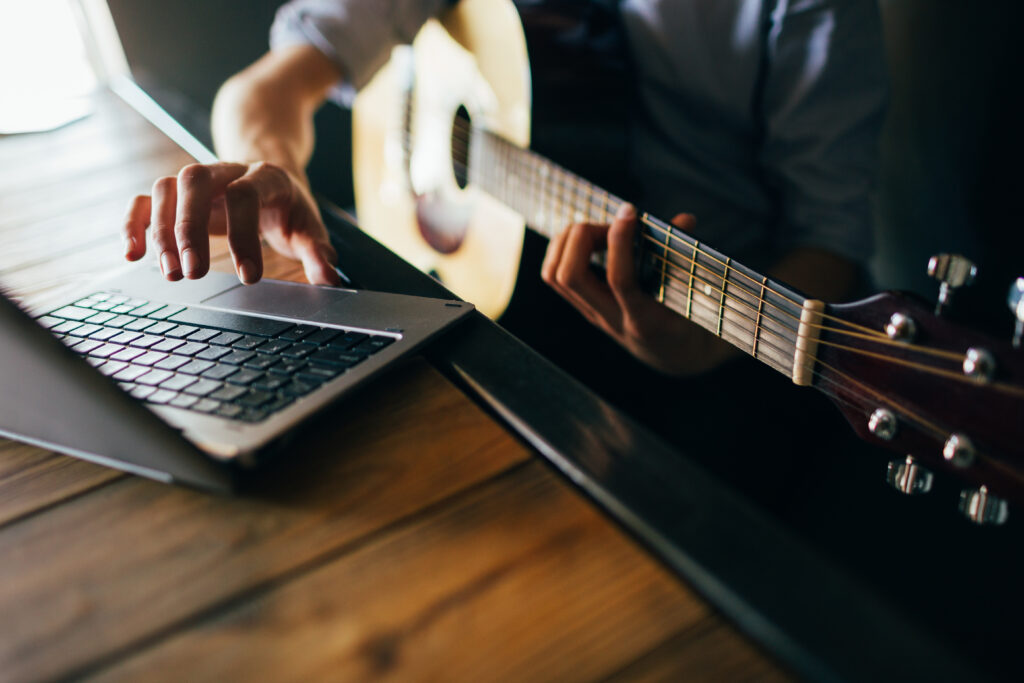 online music courses. young man learns how to play guitar through the internet. modern technology education benefits concept